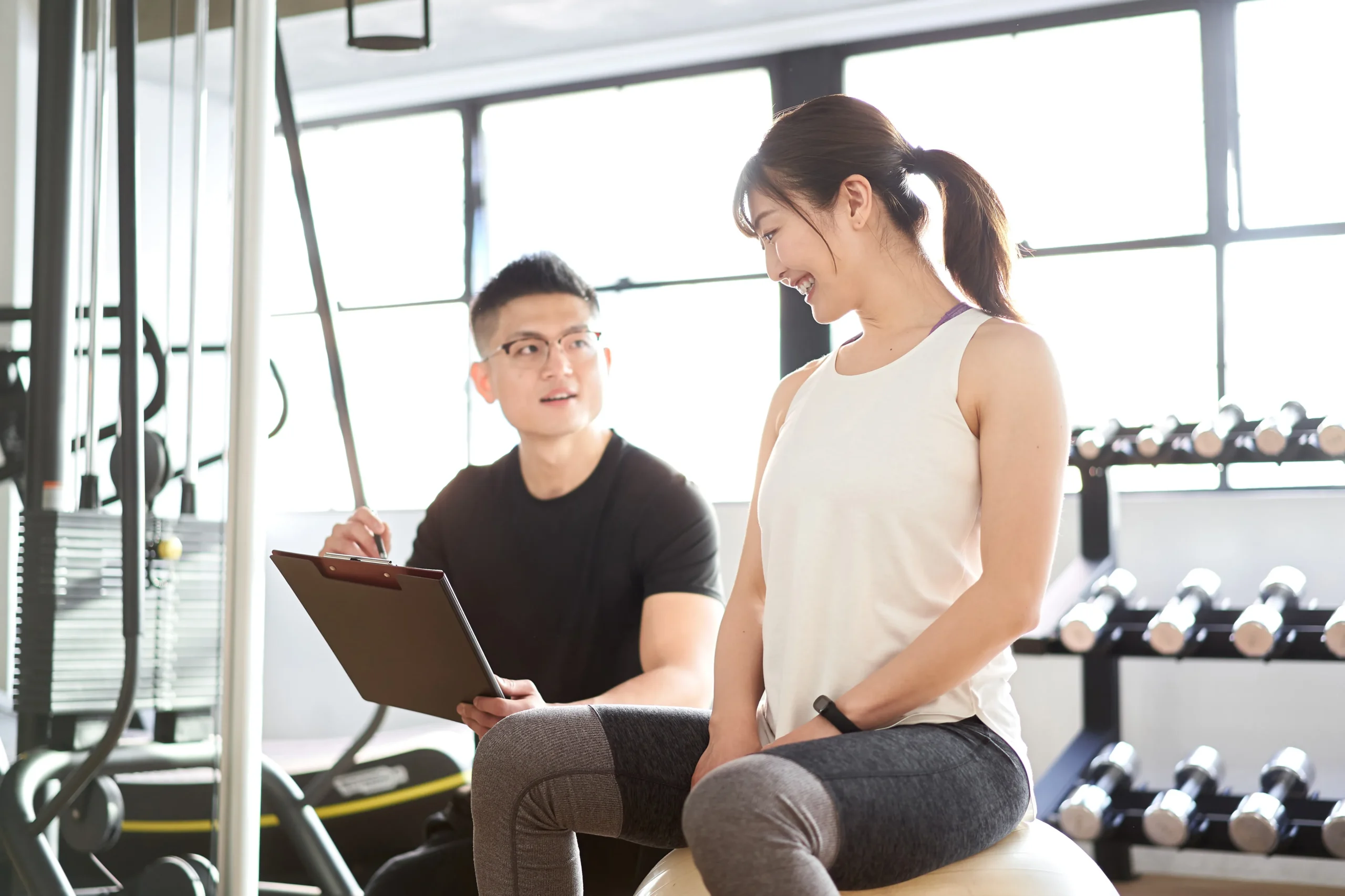 白山・本駒込のマシンピラティス×パーソナルジムSTAND TALLにて、トレーナーと笑顔で運動習慣の継続について相談する女性。