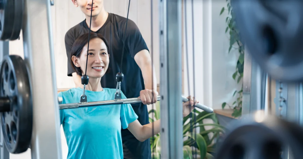 白山・本駒込のマシンピラティス×パーソナルジムSTAND TALLにて、トレーナーとラットプルダウンを行う女性