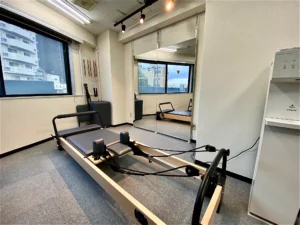 文京区白山・本駒込のマシンピラティス×パーソナルジムSTAND TALLの店舗内の様子 リフォーマーと全身鏡、スポットライトとウォータースタンドが写っている。