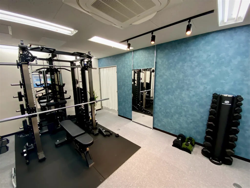 白山・本駒込のマシンピラティス×パーソナルジムSTAND TALLの店舗内の様子、スミスマシンと全身鏡、スポットライトとダンベルラックが写っている。